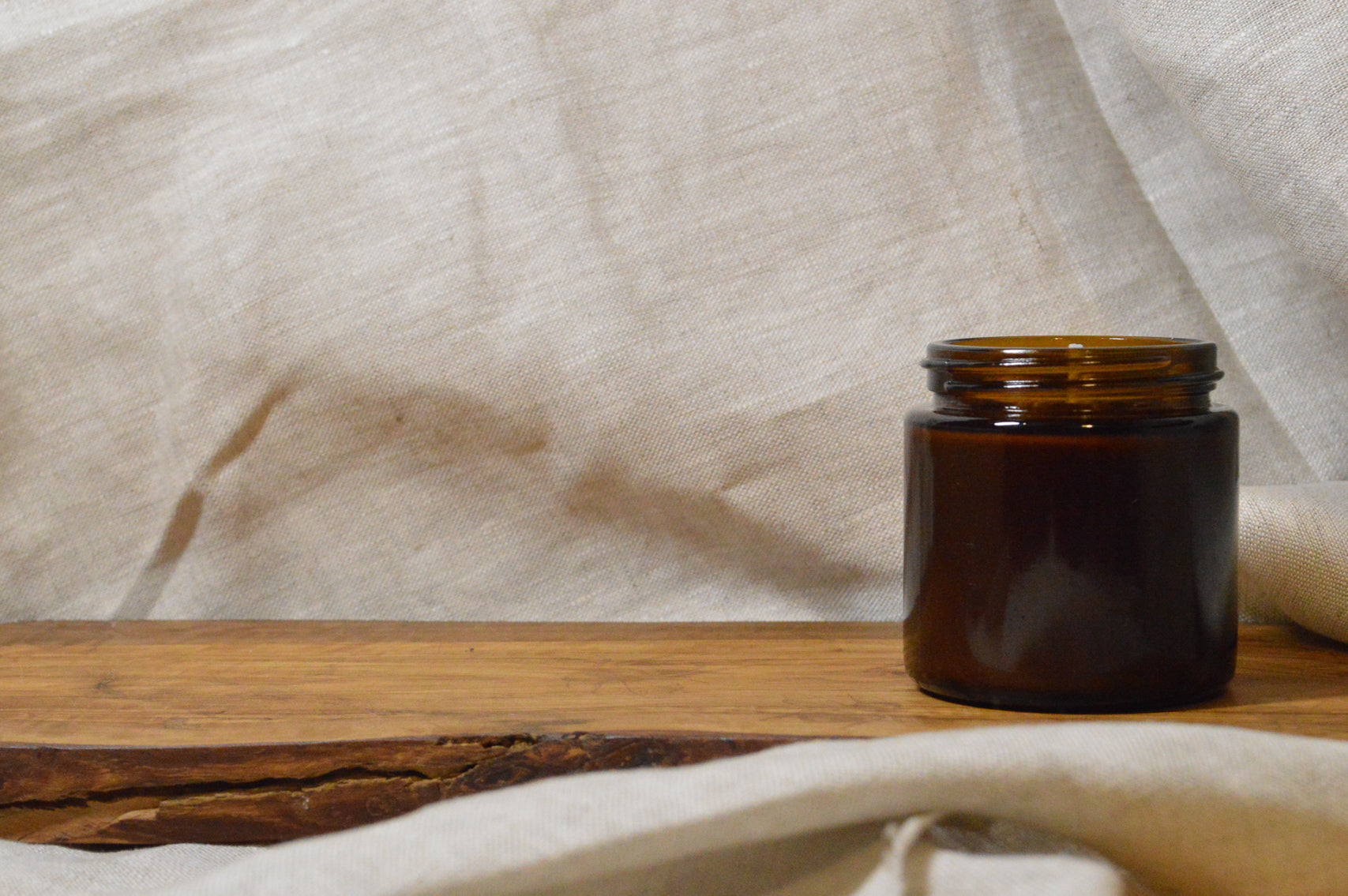 Picture is of a small brown jar on a rustic wooden shelf with a linen cloth background